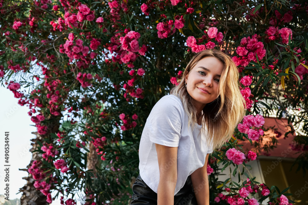 Young woman in white shirt with natural makeup standing in blooming bush Young woman in white shirt with natural makeup standing in blooming bush