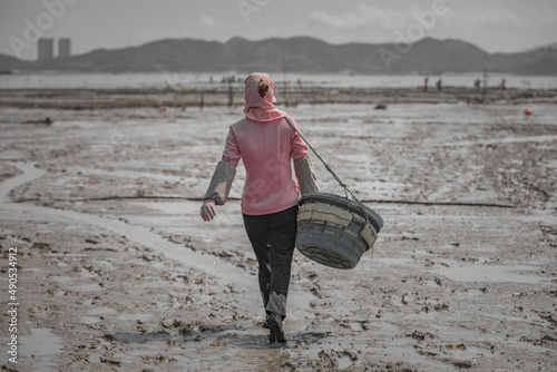 The figure of a female fisherman walking in the mud with a basket on her back photo