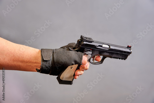 A man's hand holds a black pistol in his hand on a gray background