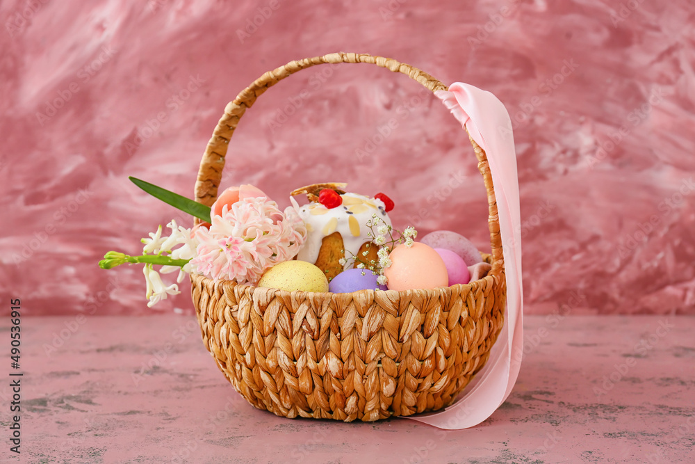 Gift basket with painted Easter eggs, flowers and cake on pink background