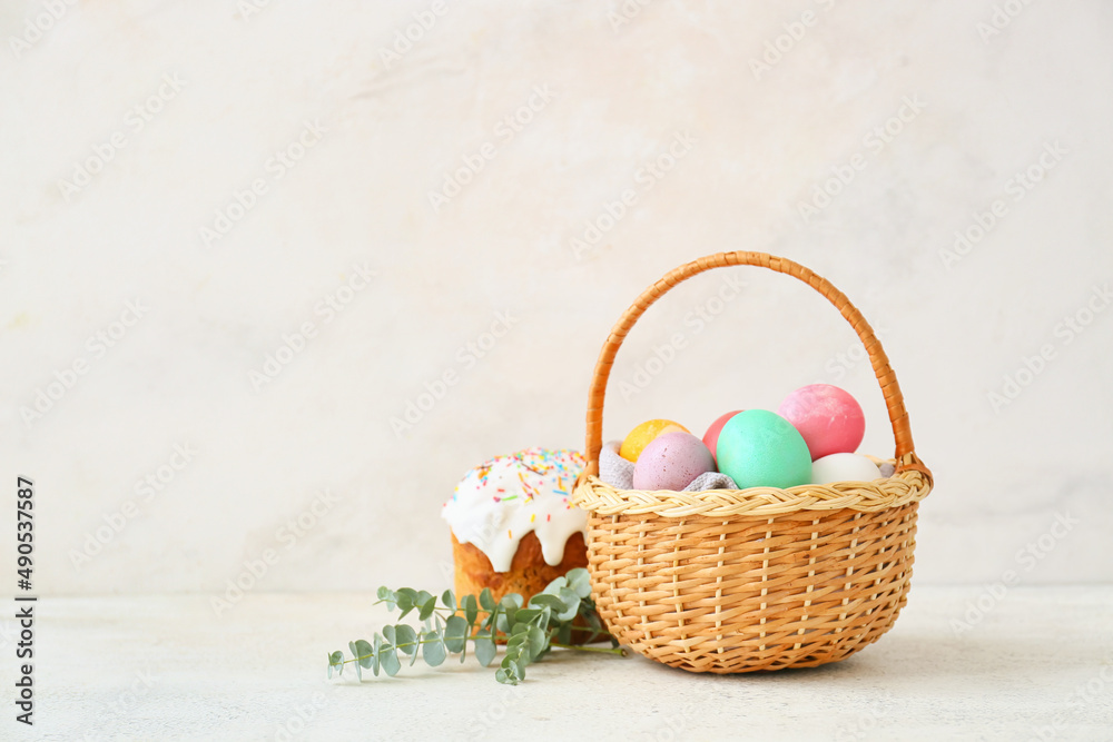 Gift basket with painted Easter eggs and cake on light background
