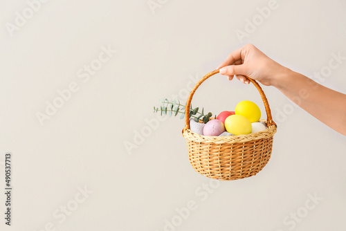 Woman holding gift basket with painted Easter eggs and cookies on light background photo