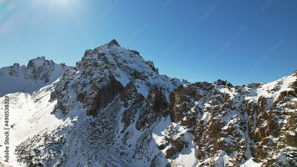 Drone view of the high snowy peaks of the Trans-Ili Alatau, Kazakhstan. Steep cliffs, glacier. Clear blue sky and sunny weather. Snow lies on rocks. Epic shooting in 4K. A place where there is no man