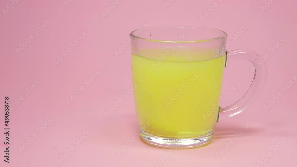 the effervescent tablet falls into the water and dissolves, vitamin orange flavor in a glass of water on a pink background the effervescent tablet falls into the water and dissolves, vitamin orange flavor in a glass of water on a pink background