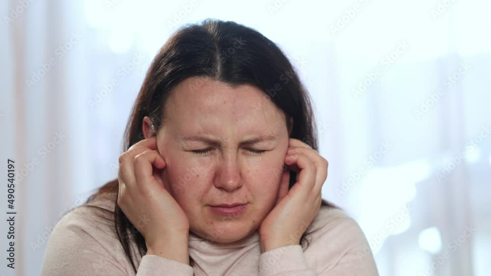 Young woman suffering of tinnitus disease, putting on her earplugs, insomnia or stress concept, sick female having an ear pain touching her painful head, healthcare Young woman suffering of tinnitus disease, putting on her earplugs, insomnia or stress concept, sick female having an ear pain touching her painful head, healthcare