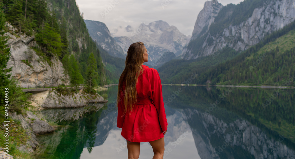 Naklejka premium Beautiful girl in a red dress in the mountains near the lake