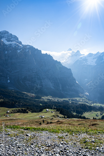A vertical image  top view of a beautiful mountain valley where the mountain peak touches the clouds  with rural villages on green meadow hills with pine trees below  in a clear blue sky with sunshine