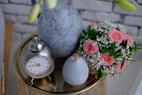 Wedding rings on a nightstand with a clock and a vase.
