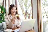 attractive Asian businesswoman using credit card for goods payments shopping online by laptop in the coffee shop. Confident and smart woman and business concept.