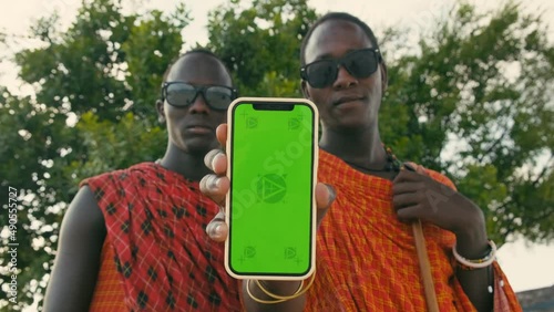 Extremely Happy, Satisfied Masai Tribe Men Showing Green Screen on Smartphone to the Camera and Making Thumb Up Sign. Masai Mara Likes New Mobile Phone App. Commercial Ad Concept.