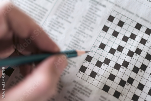 Photos Close up hand holding pencil over crossword puzzle on newspaper