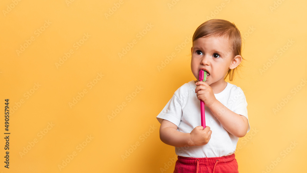 A little blonde girl brushes her teeth with toothpaste. Yellow background. A place for your text. The concept of dental hygiene. A little blonde girl brushes her teeth with toothpaste. Yellow background. A place for your text. The concept of dental hygiene.