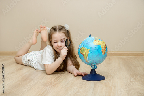 little girl lies on the floor and squints at the globe through a magnifying glass