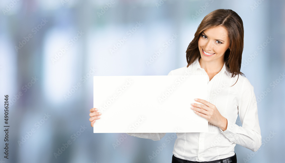 Happy smiling woman in white confident wear holding showing mock up empty signboard. Businesswoman in advertising concept. Copy space empty area. Blurred modern office background.. Happy smiling woman in white confident wear holding showing mock up empty signboard. Businesswoman in advertising concept. Copy space empty area. Blurred modern office background..