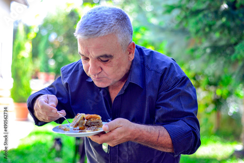 Man eating turkish baklava on a plate on sunny summer day in a backyard photo