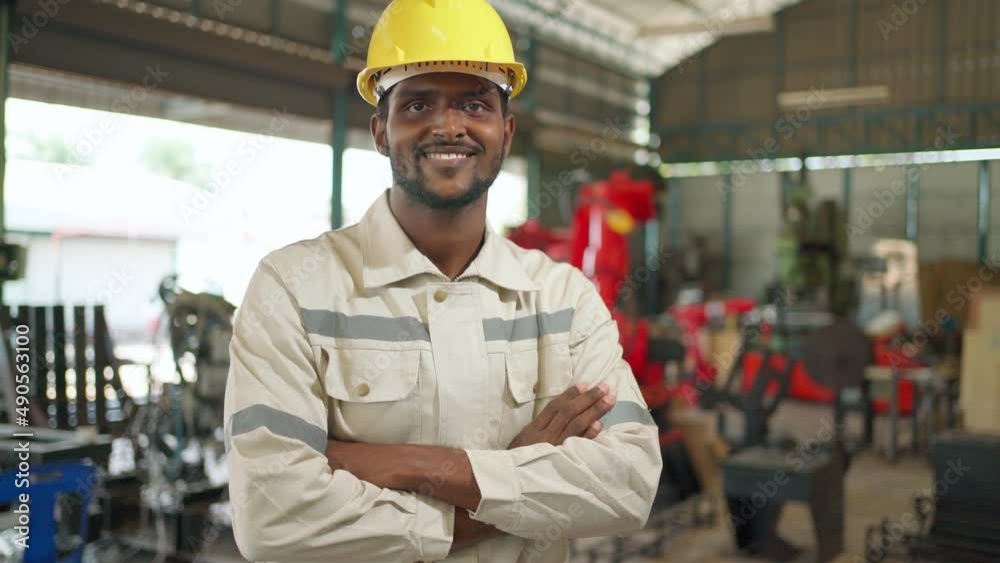 Close up portrait of confident Africa American engineer man wearing safety helmet standing in the robotic arm manufacturing. Looking forward and crossed arm. Technology and industrial concept Close up portrait of confident Africa American engineer man wearing safety helmet standing in the robotic arm manufacturing. Looking forward and crossed arm. Technology and industrial concept