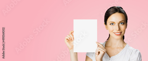 Studio portrait image of smiling woman in white cloth, hold showing demonstrate mock up paper signboard. Business and advertising concept. Copy space empty free area for text. Rose pink background.
