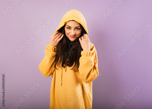 Relaxing thinking smiling sporty woman posing in fashion yellow hoodie on purple bright background with empty copy space. Happy