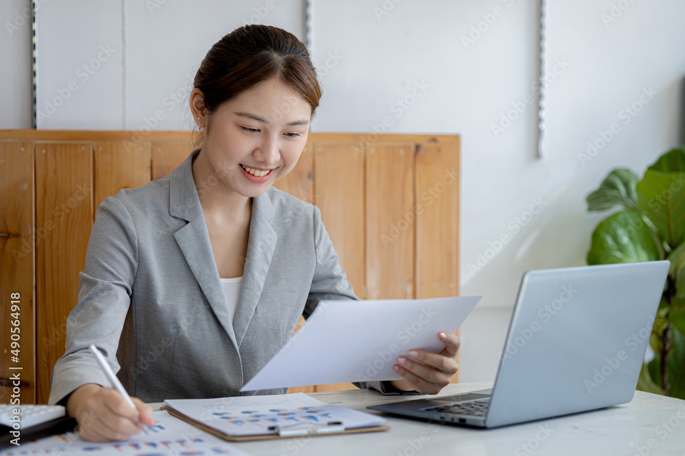 A beautiful Asian businesswoman sitting in her private office, she is checking company financial documents, she is a female executive of a startup company. Concept of financial management. A beautiful Asian businesswoman sitting in her private office, she is checking company financial documents, she is a female executive of a startup company. Concept of financial management.