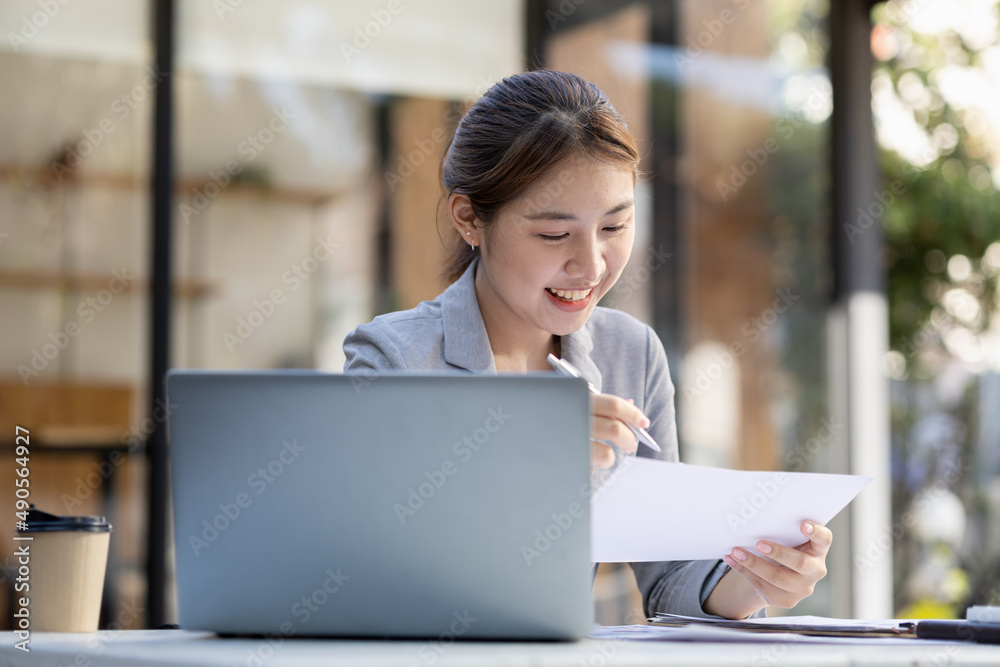A beautiful Asian businesswoman sitting in her private office, she is checking company financial documents, she is a female executive of a startup company. Concept of financial management. A beautiful Asian businesswoman sitting in her private office, she is checking company financial documents, she is a female executive of a startup company. Concept of financial management.