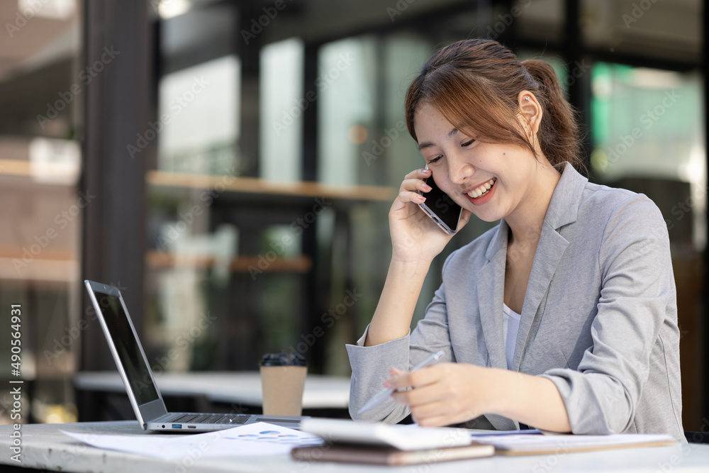 Asian woman talking on the phone, she is a salesperson in a startup company, she is calling customers to sell products and promotions. Concept of selling products through telephone channels. Asian woman talking on the phone, she is a salesperson in a startup company, she is calling customers to sell products and promotions. Concept of selling products through telephone channels.