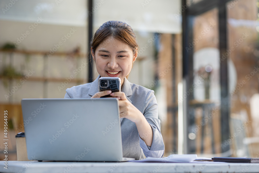 Fototapeta premium young businesswoman looking at financial information from a mobile phone, she is checking company financial documents, she is a female executive of a startup company. Concept of financial management.