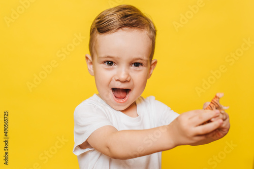 Portrait of a cute laughing little boy on a yellow background with a toy in his hands. Copy space.