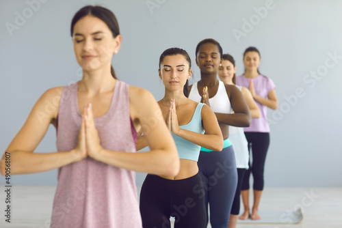 Calm serene sporty young woman standing with folded arms in a gesture of namaste in a group yoga class. Concept of meditation, spirituality and healthy lifestyle. Selective focus. © Studio Romantic