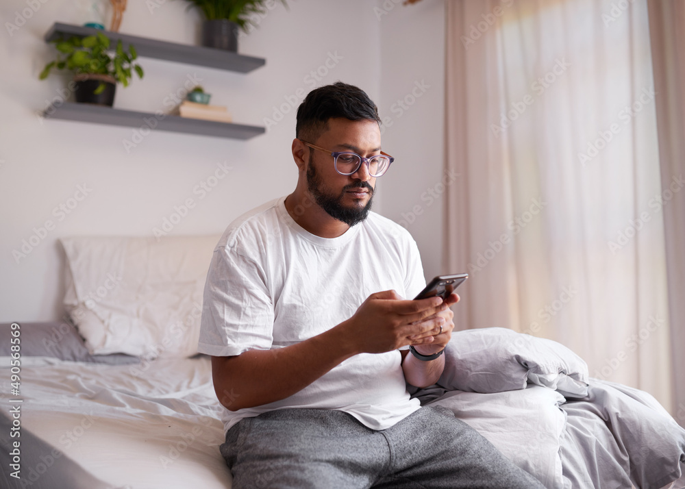 A man sits on the end of his bed looking at his mobile phone in the morning A man sits on the end of his bed looking at his mobile phone in the morning
