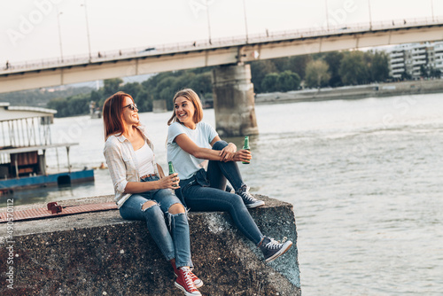 Two female friends are sitting on dock ,relaxing and drinking beer. 