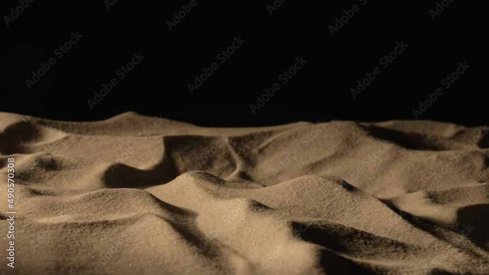 Camera pans over mound of dry sand in dark on black background. Close up shot of sandy dune with grainy particles sparkling in the light. Slow motion ready, 4K at 59.97fps.