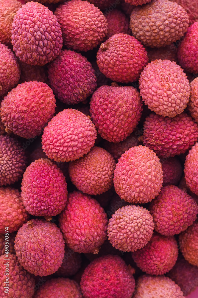 many ripe red unpeeled lychees - vertical food background