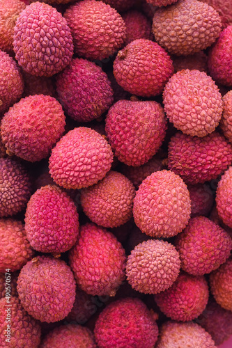 many ripe red unpeeled lychees - vertical food background