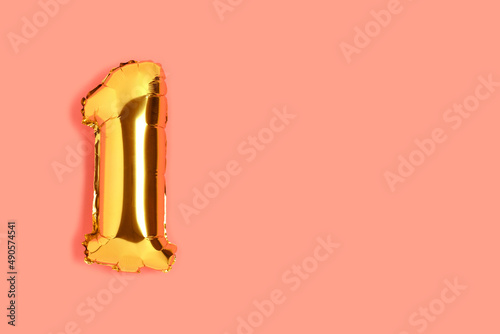 Number 1 golden balloon with copyspace. One year anniversary celebration concept on a coral colored background.