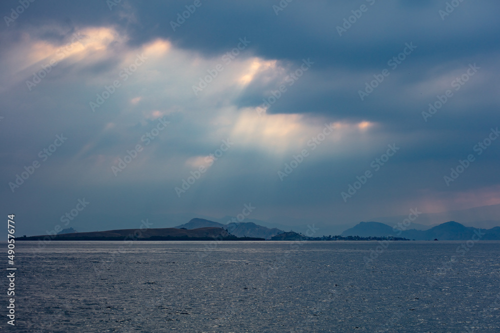Sunlight pierces low clouds that drift over Komodo National Park, Indonesia. This region has an annual dry and a wet season. Sunlight pierces low clouds that drift over Komodo National Park, Indonesia. This region has an annual dry and a wet season.