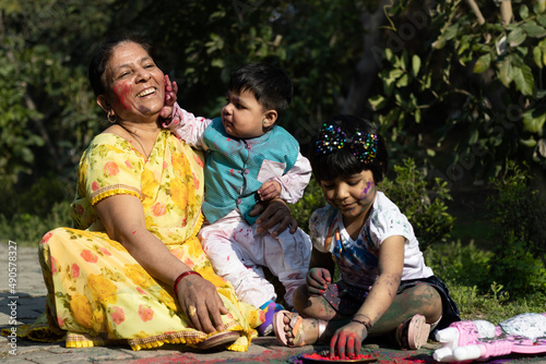 Happy Asian Indian Kids Boy, Girl And Grandmother Multi Generation Enjoying The Festival Of Colors With Holi Color Powder Called Gulal Or Rang