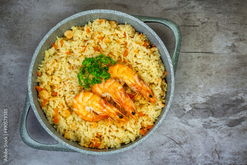 Rice with shrimps in a frying pan on a wooden table, top view.