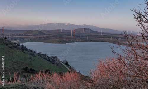 View of Bental water reservoir  the Golan hills with wind turbines and the Hermon Mountain Range at sunset as seen from Mount Bental summit  Golan Heights  Israel.