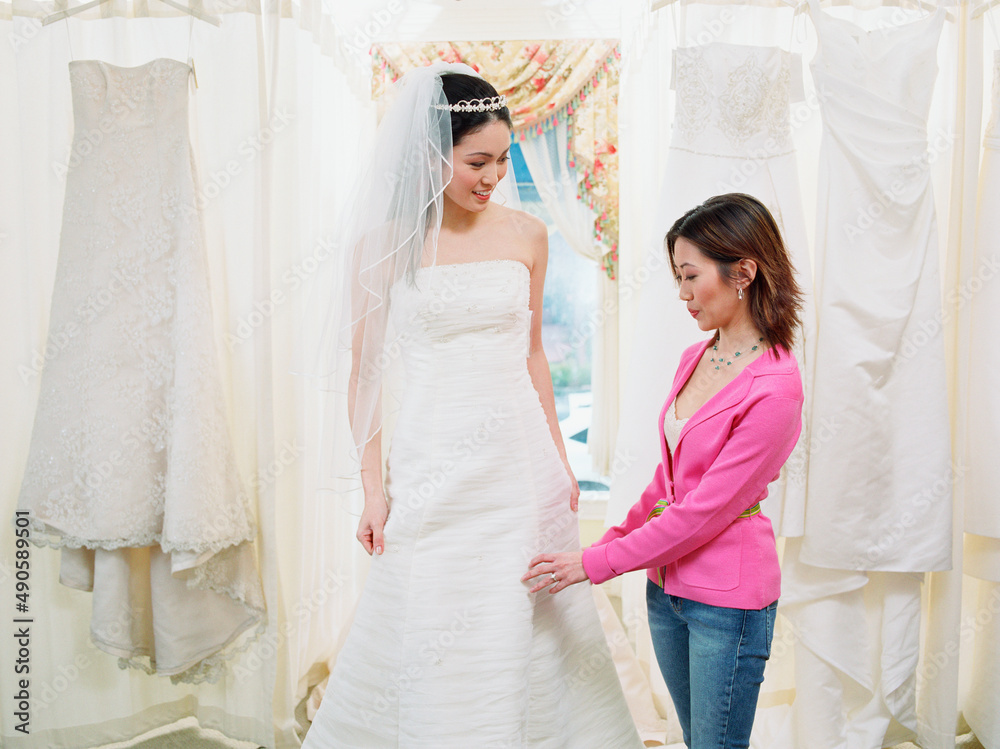 Young woman helping bride-to-be try on her gown Young woman helping bride-to-be try on her gown
