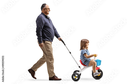 Full length profile shot of a grandfather pushing a girl on a tricycle