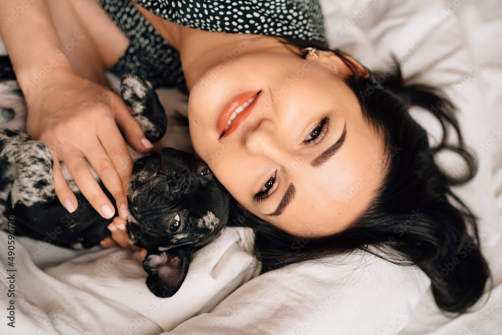 top view. happy pretty brunette woman with a French Bulldog puppy in a bed. top view. happy pretty brunette woman with a French Bulldog puppy in a bed.