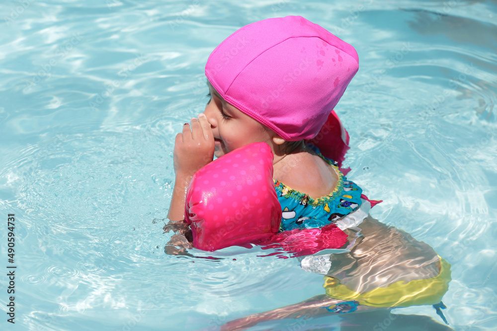 Child in the pool swimming with pink float with blue water.