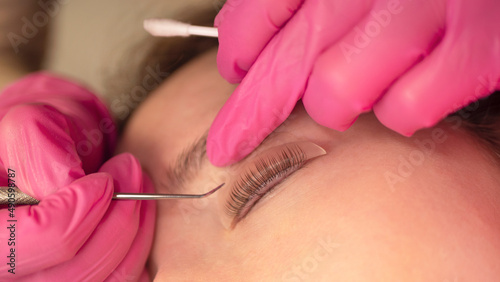 Woman on the procedure for eyelash extensions, lamination in beauty salon. Cosmetologist applying glue on woman's lashes. Close-up of girl face during lash lift laminating botox set.  photo
