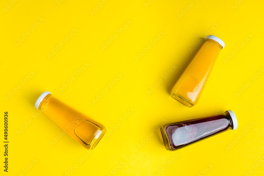 Bottles with yellow and red liquid halthy beverage on yellow background. Orange apple cherry juice Bottles with yellow and red liquid halthy beverage on yellow background. Orange apple cherry juice