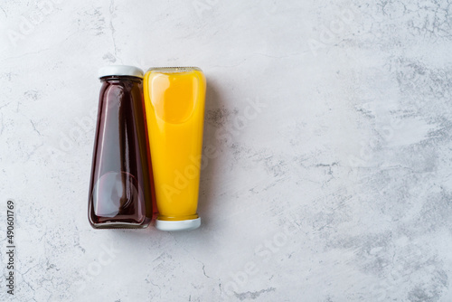 Bottles with yellow and red liquid halthy beverage on yellow background. Orange and cherry juice