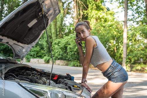 beautiful girl wear short shorts and t-shirts  looking into engine compartment of broken down car photo