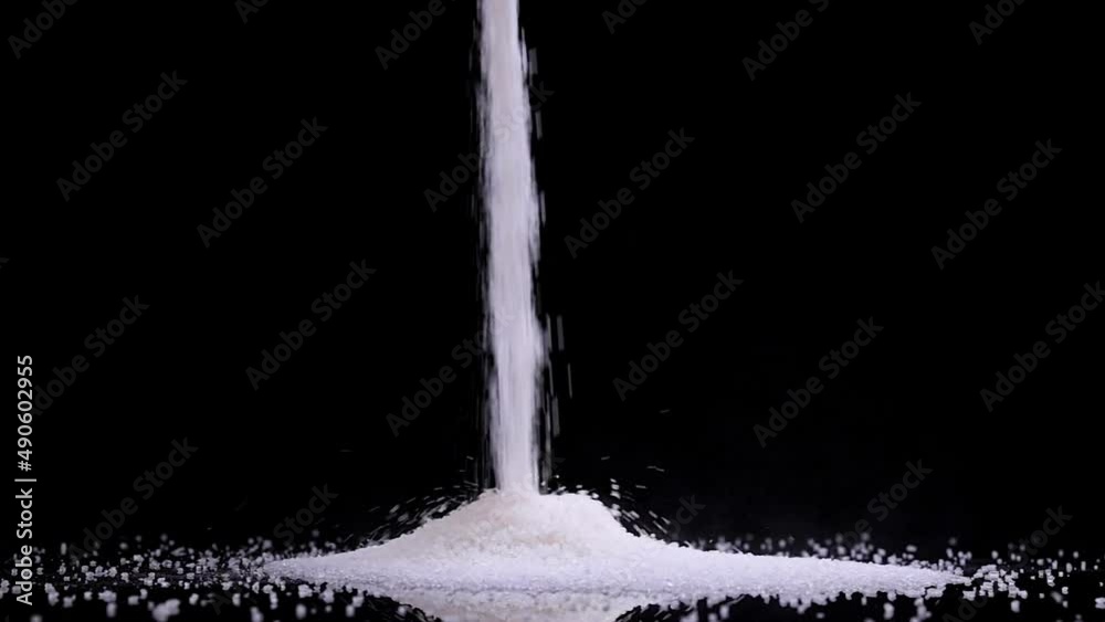 Pouring white sugar on black background in slow motion. The benefits or the danger of sugar consumption to health concept.