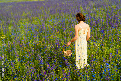 Foto Scena con una donna girata di spalle con un cesto nella mano in un campo fiorito a giugno a Castelluccio di Norcia in Italia