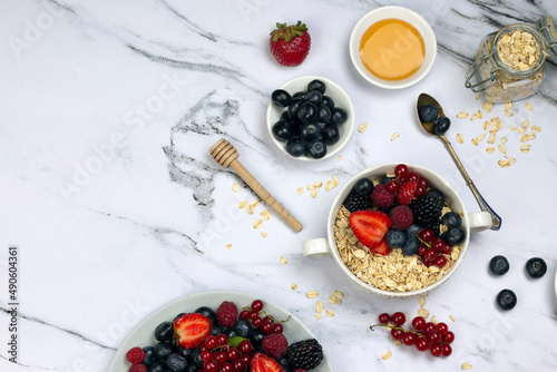 Healthy breakfast or snack, oat with berry, honey and ripe sweet berries on white marble table. top wave, flat lay.