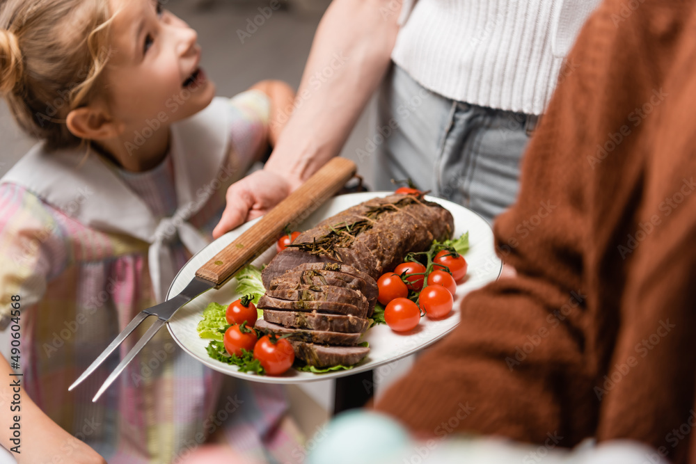 woman holding plate with meat and fresh vegetables near excited daughter.